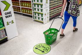 A shopper pulls a shopping basket past a floor sticker advising customers to maintain the British government's current social distancing guidelines. (Photo by TOLGA AKMEN/AFP via Getty Images)