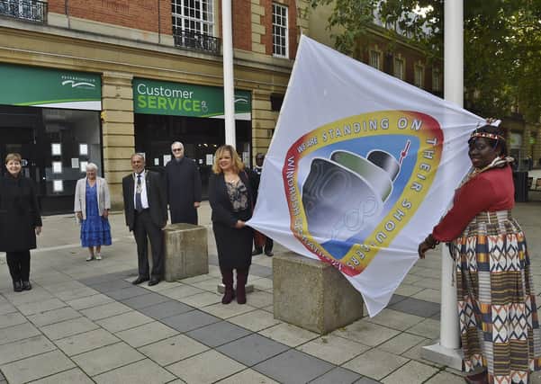 Julie Davidson and Bernadetta Omondi raising the Windrush flag at Bridge Street watched by Peterborough City Council officials for the start of Black History Month.