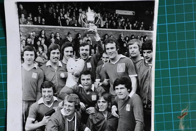 John Cozens holds the 1973-74 Fourth Division champions trophy aloft in the middle of his happy teammates.