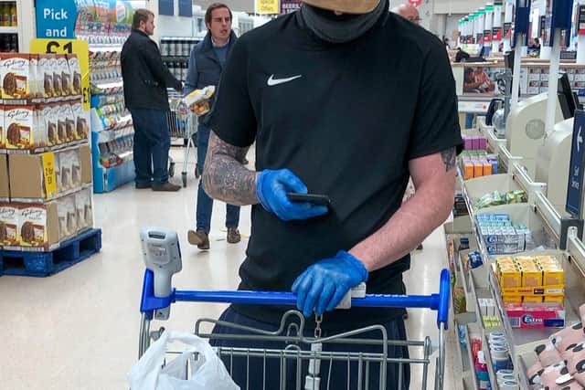 A man with a trolley wears protective gloves as he queues at the checkout of a Tesco store in Peterborough. Picture: Joe Giddens/PA Wire