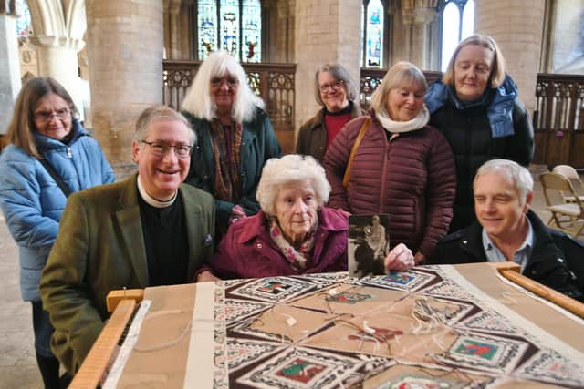 Vice Dean Tim Alban-Jones with Dawn Large (88) and son Maurice Large admiring the Peterborough Cathedral nave tapestry with members of  the Sacristy Stitchers. Mrs Large holds a photo of her aunt, Madeleine Freeman, who initiated the tapestry project in 1986.