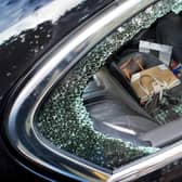 A smashed side window of a car broken during a robbery.  Showing hand bags and a camera on the back seat about to be stolen.