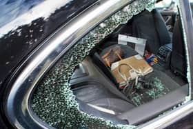 A smashed side window of a car broken during a robbery.  Showing hand bags and a camera on the back seat about to be stolen.