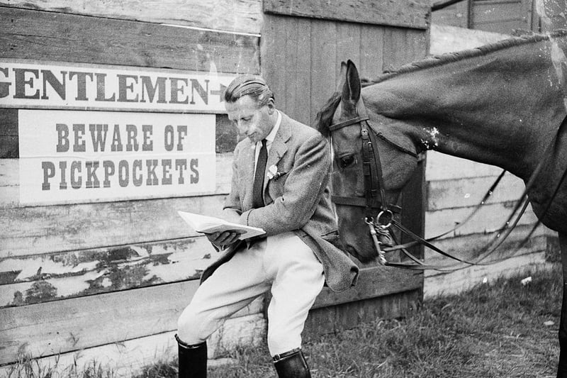 A man standing in front of a sign warning of pickpockets at the Peterborough agricultural show while a horse rummages through his pockets on 18th July 1956: