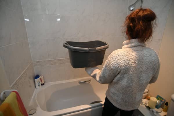 A Peterborough single mum-of-two pictured holding the bucket she fills with warm water from her kettle to bathe her two children in.