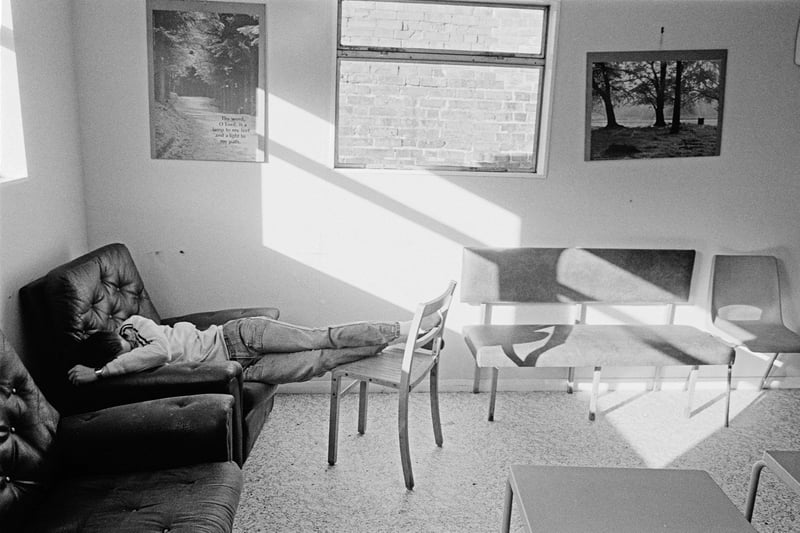 A young unemployed man sleeps under a religious poster as light streams in through the window of the Westgate Project building in Peterborough, August 1985.