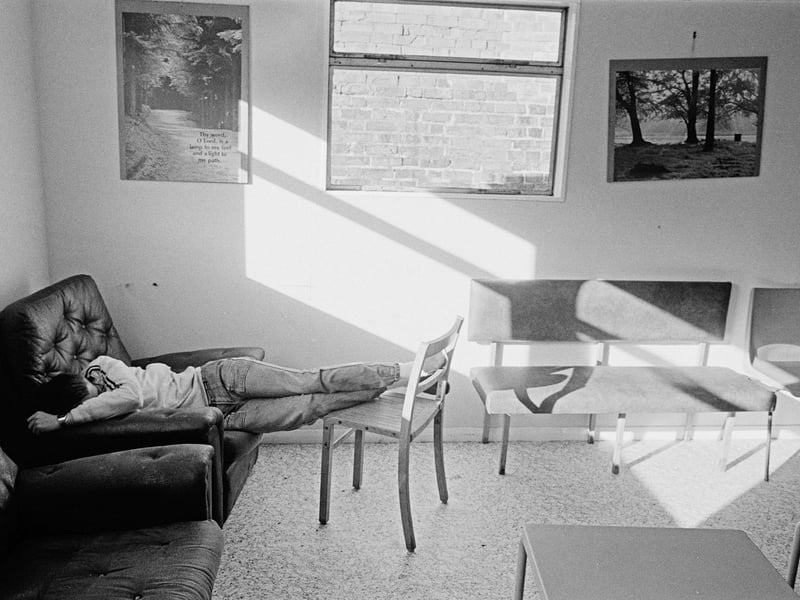 A young unemployed man sleeps under a religious poster as light streams in through the window of the Westgate Project building in Peterborough, August 1985.