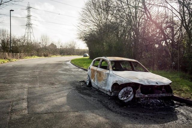 A burnt-out car left abandoned at the road side of a quiet rural location.