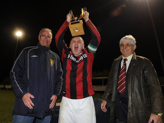 Netherton captain Aidan Stanford lifts the cup from Hunts FA official Alan Poulain and (right), Peterborough Sunday Afternoon League Chairman Mario Storti, at Chestnut Avenue.