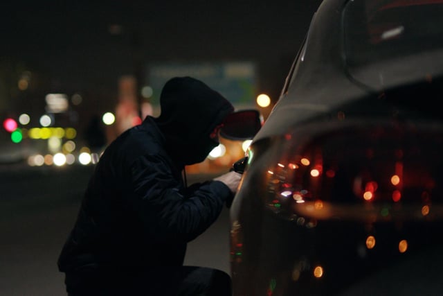 A thief shines a flashlight into a car.